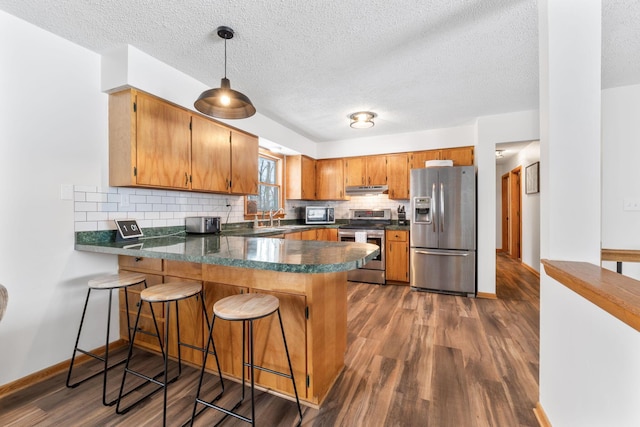 kitchen with sink, decorative backsplash, kitchen peninsula, stainless steel appliances, and dark wood-type flooring