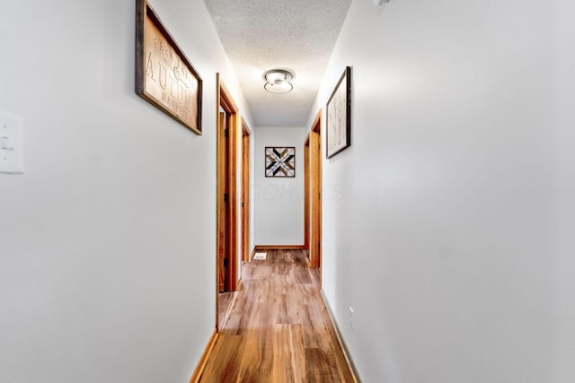 corridor with light hardwood / wood-style floors and a textured ceiling