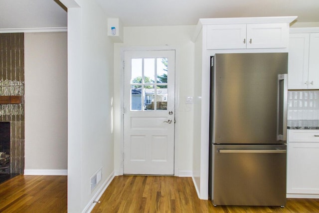 interior space featuring backsplash, dark stone countertops, white cabinetry, hardwood / wood-style flooring, and stainless steel fridge