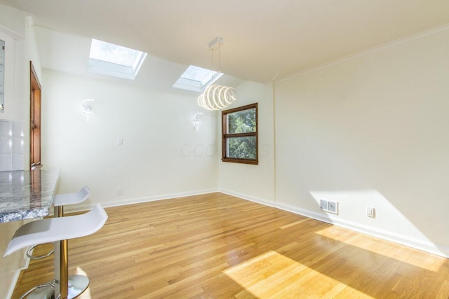 unfurnished dining area featuring a skylight, ornamental molding, and hardwood / wood-style flooring