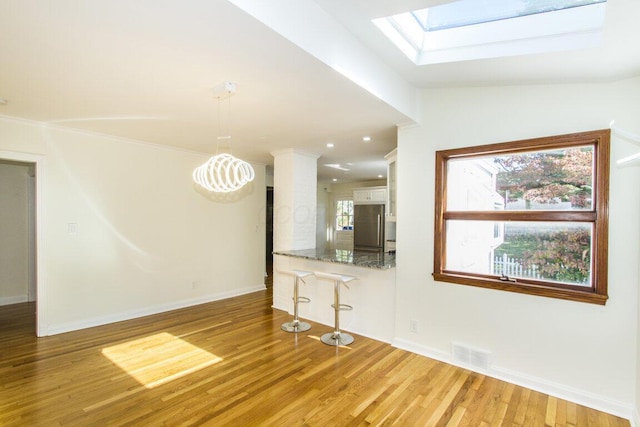 unfurnished living room featuring light wood-type flooring, vaulted ceiling with skylight, and a healthy amount of sunlight