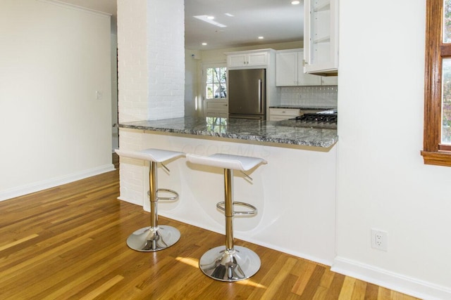 kitchen with tasteful backsplash, dark stone countertops, a breakfast bar, stainless steel refrigerator, and white cabinets