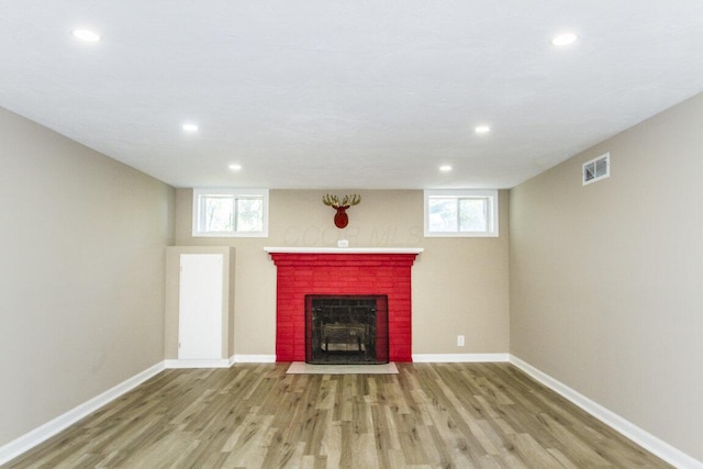 unfurnished living room with a healthy amount of sunlight, a brick fireplace, and light hardwood / wood-style flooring