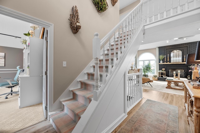 stairs featuring hardwood / wood-style flooring, a towering ceiling, and a fireplace