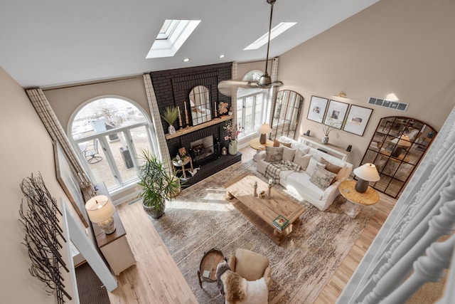 living room with a brick fireplace, a skylight, high vaulted ceiling, and light wood-type flooring