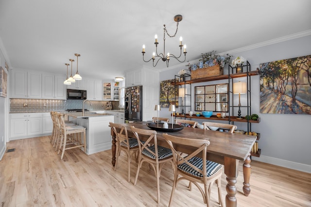 dining space featuring a notable chandelier, sink, ornamental molding, and light hardwood / wood-style floors