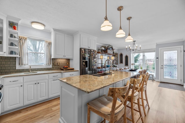 kitchen featuring fridge with ice dispenser, sink, white cabinetry, and a center island with sink