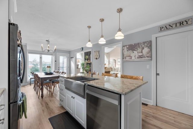 kitchen with decorative light fixtures, appliances with stainless steel finishes, an island with sink, light stone countertops, and white cabinets