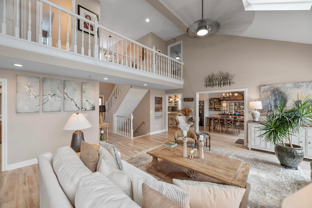 living room with a skylight, light hardwood / wood-style flooring, ceiling fan, and a high ceiling