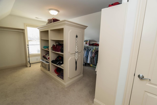 walk in closet with light colored carpet and vaulted ceiling