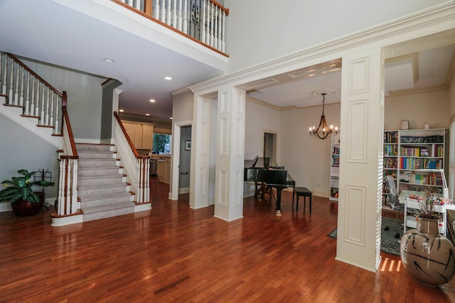 foyer entrance with decorative columns, dark hardwood / wood-style floors, crown molding, and a chandelier