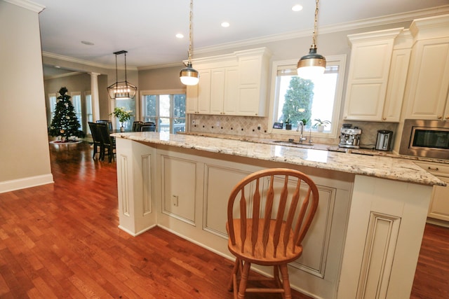 kitchen with a kitchen island, light stone counters, hanging light fixtures, and sink