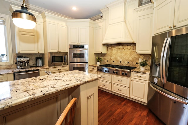 kitchen with premium range hood, pendant lighting, crown molding, appliances with stainless steel finishes, and light stone counters