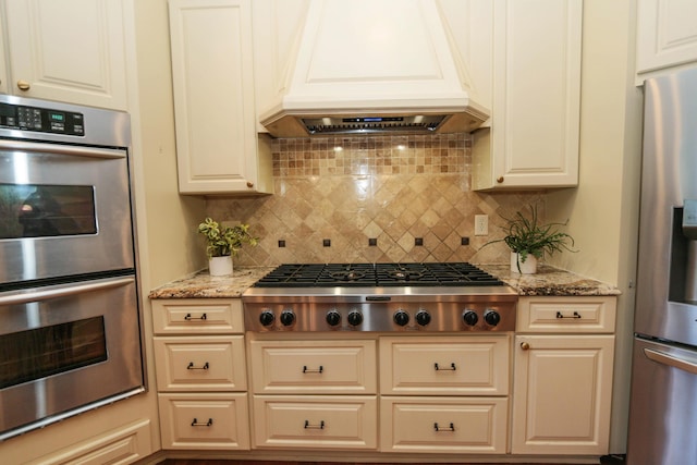 kitchen featuring light stone countertops, stainless steel appliances, backsplash, and custom range hood