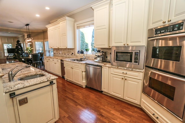 kitchen with appliances with stainless steel finishes, sink, hanging light fixtures, and light stone countertops