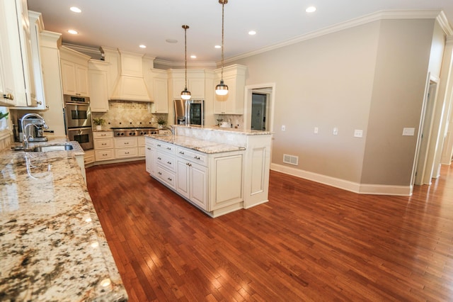 kitchen featuring light stone countertops, appliances with stainless steel finishes, decorative light fixtures, sink, and custom range hood