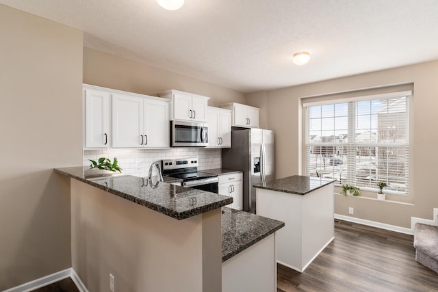 kitchen with appliances with stainless steel finishes, white cabinetry, backsplash, dark stone countertops, and kitchen peninsula