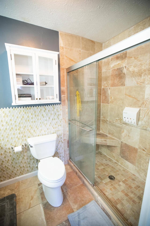 bathroom with toilet, tile walls, a shower with shower door, and a textured ceiling