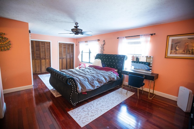 bedroom featuring a textured ceiling, ceiling fan, two closets, and dark hardwood / wood-style floors