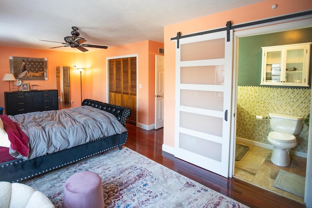 bedroom featuring a barn door, ceiling fan, connected bathroom, a closet, and dark wood-type flooring