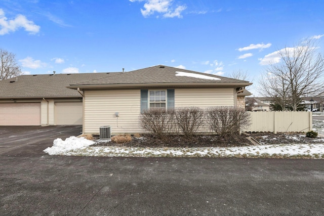 view of side of property with driveway, central AC unit, roof with shingles, and fence