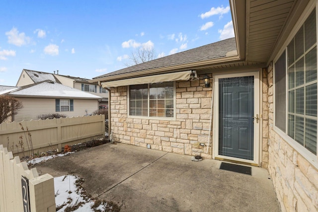 doorway to property with a shingled roof, stone siding, a patio area, and fence