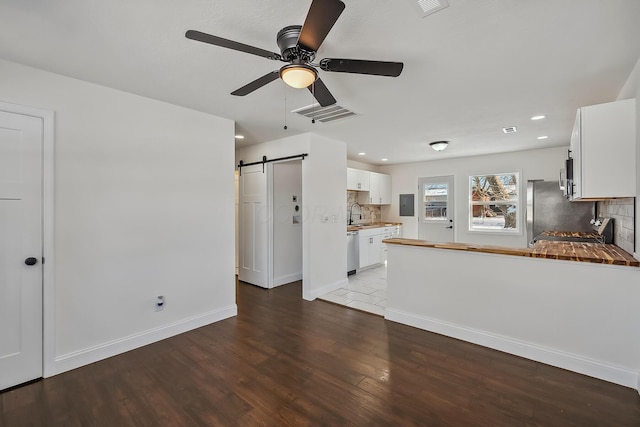 unfurnished living room featuring sink, light wood-type flooring, ceiling fan, electric panel, and a barn door