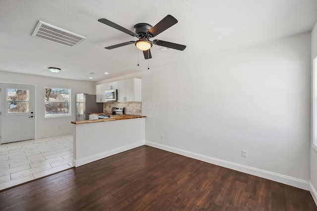 interior space featuring butcher block countertops, decorative backsplash, kitchen peninsula, stainless steel appliances, and white cabinets