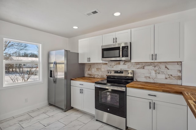 kitchen featuring butcher block countertops, decorative backsplash, stainless steel appliances, and white cabinetry