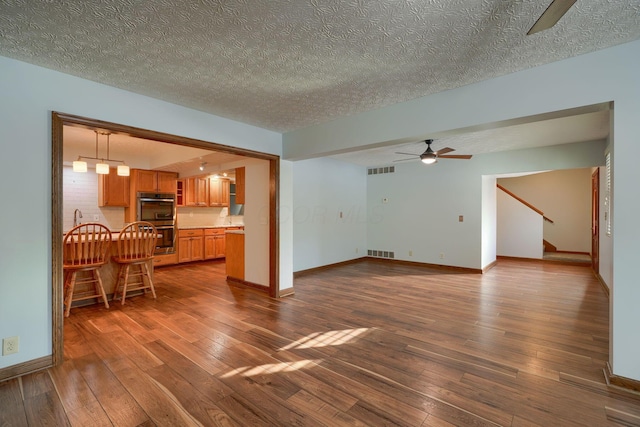 unfurnished living room featuring sink, a textured ceiling, dark hardwood / wood-style floors, and ceiling fan