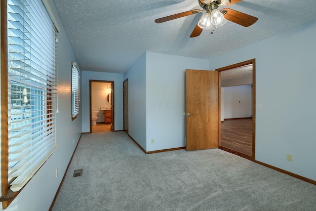 unfurnished bedroom featuring ceiling fan, light colored carpet, and ensuite bath