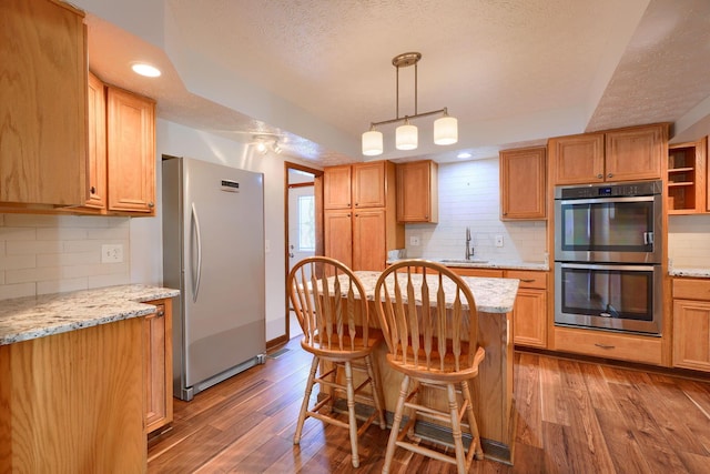 kitchen with a kitchen island, a kitchen bar, stainless steel appliances, sink, and light stone counters