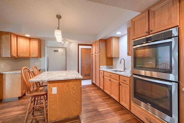 kitchen featuring hanging light fixtures, sink, a kitchen island, dark hardwood / wood-style flooring, and stainless steel appliances