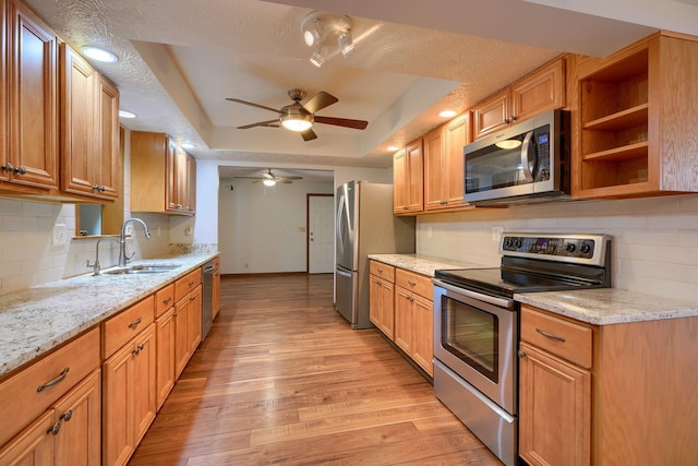 kitchen featuring light hardwood / wood-style flooring, a raised ceiling, sink, light stone counters, and stainless steel appliances