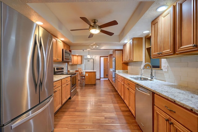 kitchen featuring light hardwood / wood-style flooring, appliances with stainless steel finishes, sink, light stone countertops, and a tray ceiling