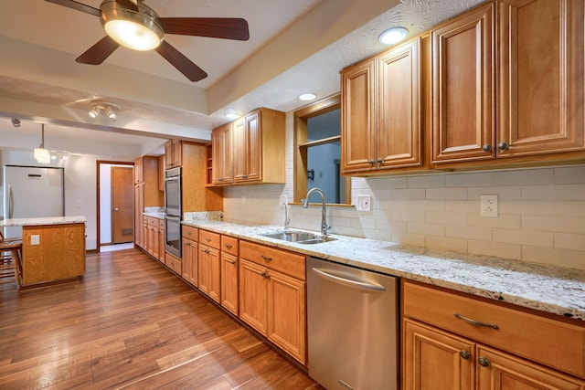 kitchen featuring wood-type flooring, stainless steel appliances, decorative backsplash, sink, and light stone counters