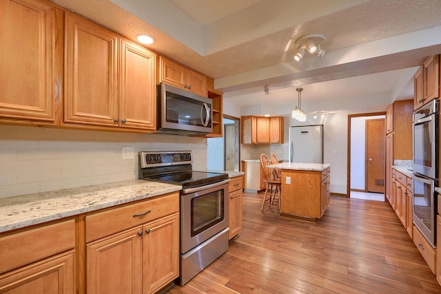 kitchen with appliances with stainless steel finishes, a kitchen island, tasteful backsplash, light hardwood / wood-style floors, and light stone counters