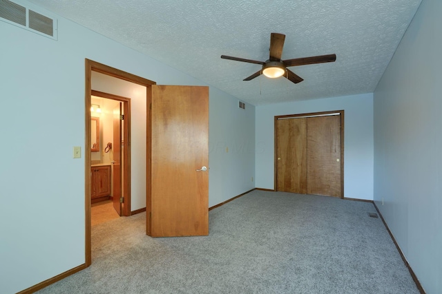 unfurnished bedroom featuring ceiling fan, a textured ceiling, a closet, and light carpet