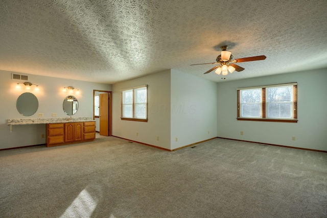 unfurnished living room with ceiling fan, light colored carpet, a textured ceiling, and built in desk