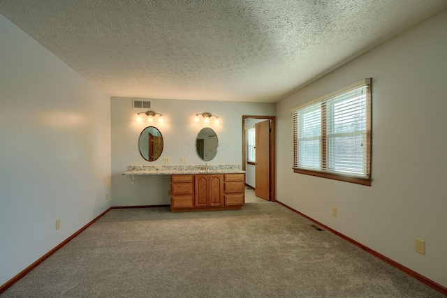 unfurnished bedroom with built in desk, a textured ceiling, and light carpet