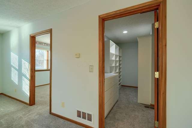 corridor featuring a textured ceiling and light carpet