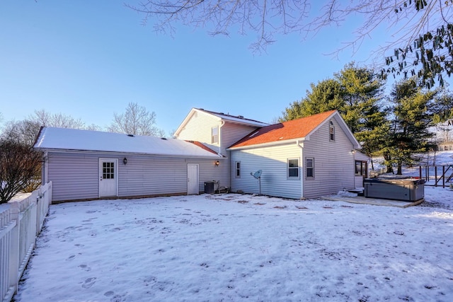 snow covered rear of property featuring cooling unit and a hot tub