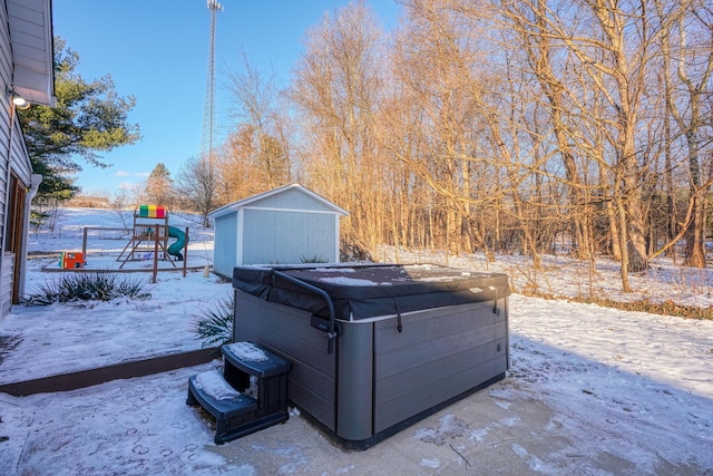 snowy yard with a storage shed, a hot tub, and a playground