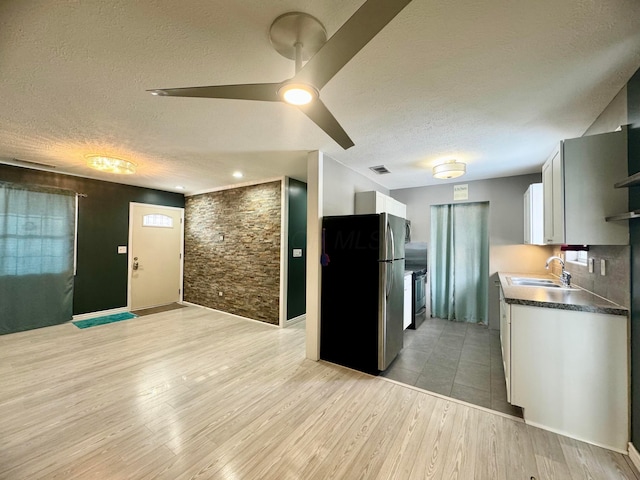 kitchen featuring visible vents, light wood-style floors, freestanding refrigerator, a sink, and a textured ceiling