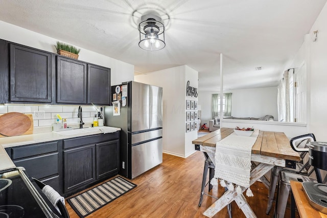 kitchen with sink, stainless steel fridge, backsplash, and light hardwood / wood-style flooring