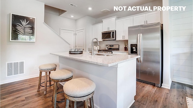 kitchen featuring a kitchen bar, light stone counters, appliances with stainless steel finishes, dark hardwood / wood-style flooring, and white cabinets