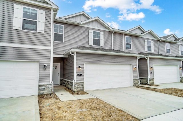 multi unit property featuring a garage, stone siding, and driveway