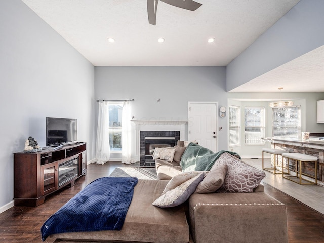 living room featuring ceiling fan, a tile fireplace, dark hardwood / wood-style flooring, and a textured ceiling