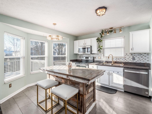 kitchen featuring decorative light fixtures, backsplash, white cabinetry, and appliances with stainless steel finishes