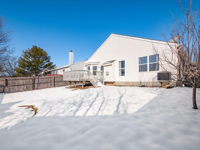 snow covered back of property with a deck and cooling unit